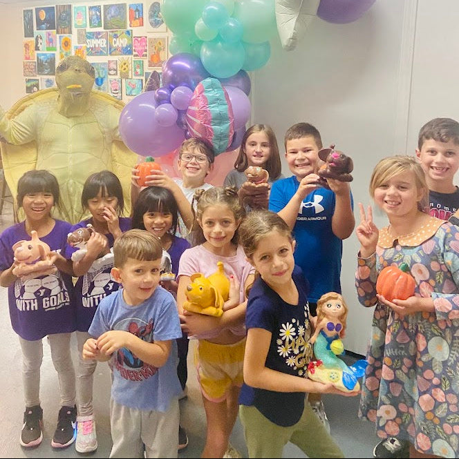 Children posing with balloons and toys in a classroom setting